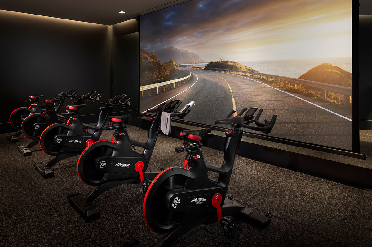an indoor cycling spin room with a large screen on the wall  inspired by equinox fitness and wellness design
